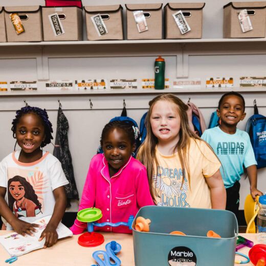 four children smiling at school with a project in front of them.