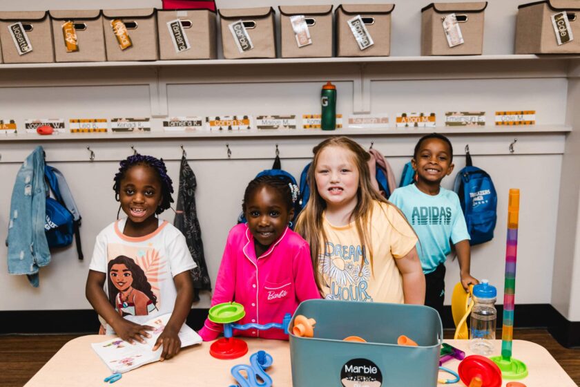 four children smiling at school with a project in front of them.