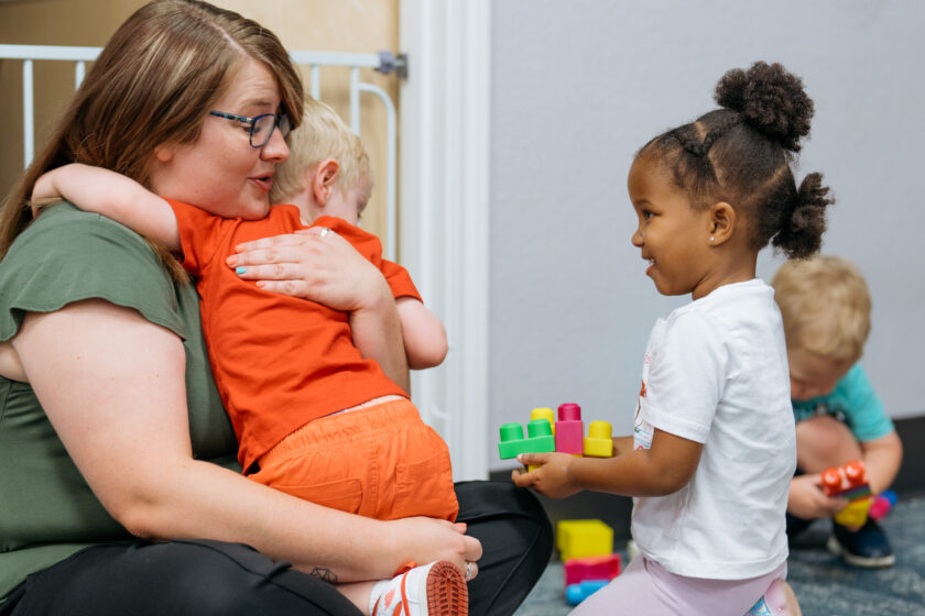 Woman hugging child wearing an orange shirt.