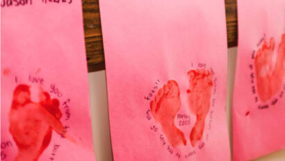Children's drawings on pink paper hung up on a wall.