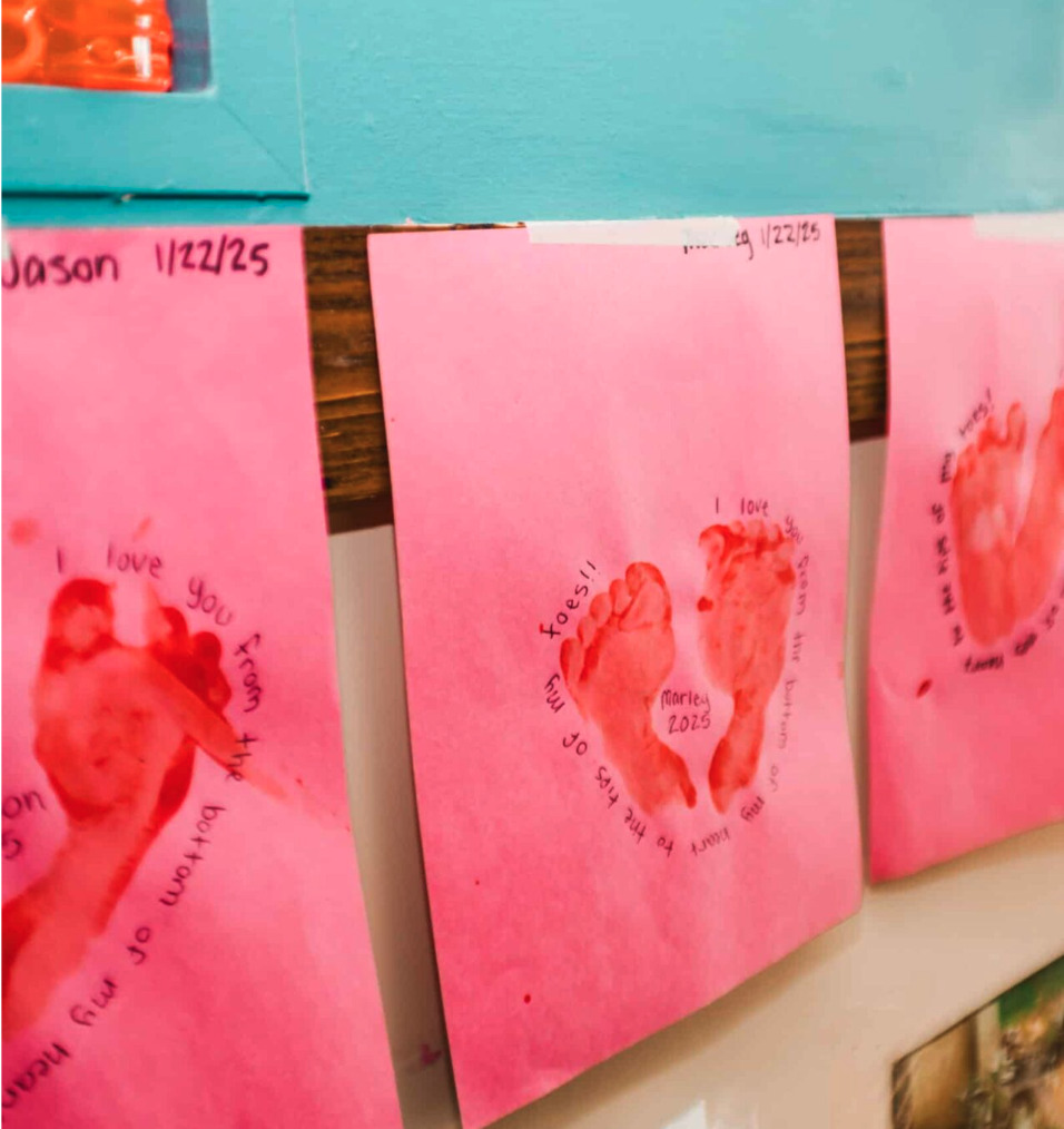 Children's drawings on pink paper hung up on a wall.