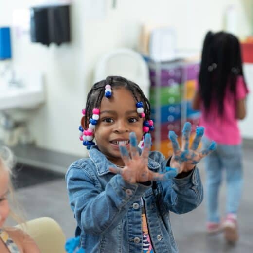 Child smiling and holding up hands covered in blue paint.