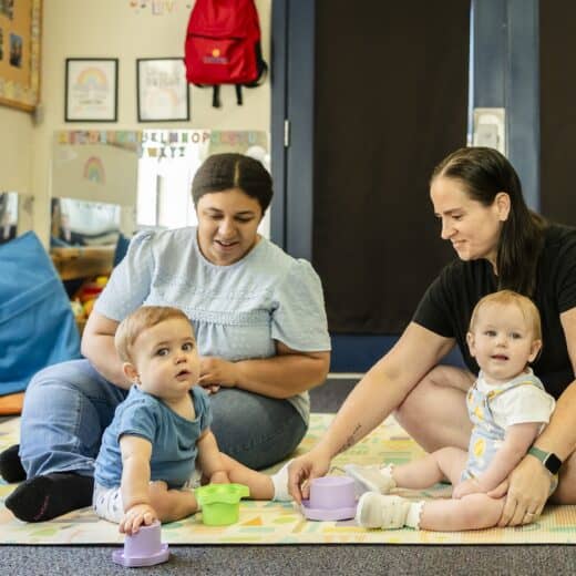 Two woman and two babies sitting on a rug playing.